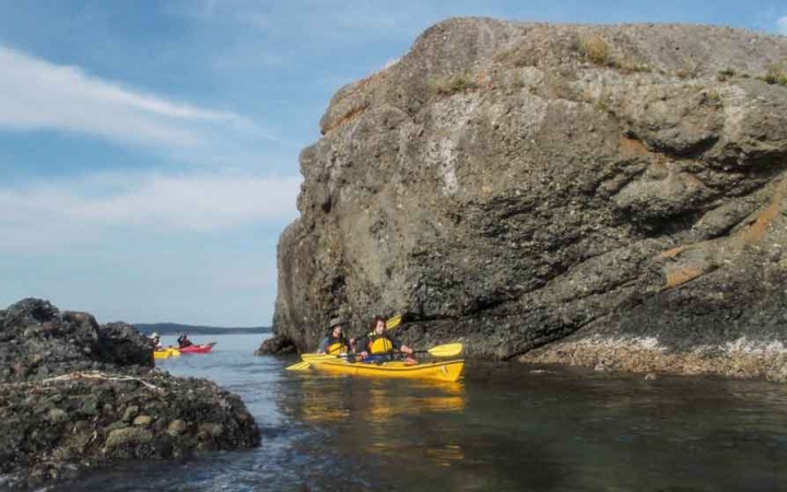 two people in a yellow kayak paddle between two rock formations on an outward bound course